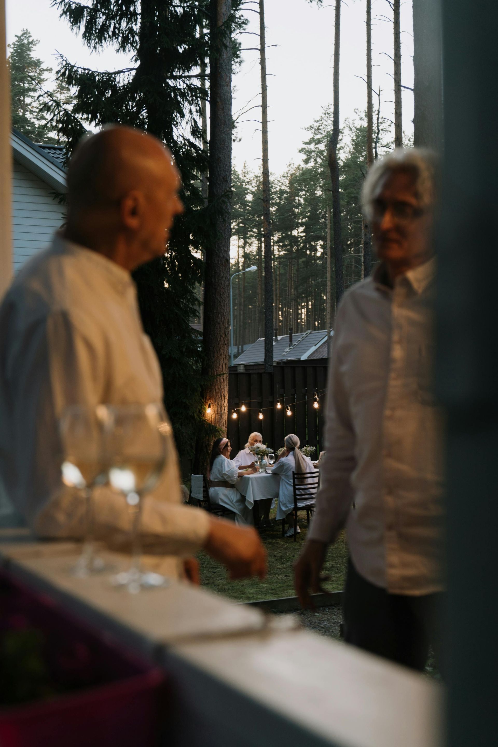 To menn samtaler på verandaen; et middagsselskap er i bakgrunnen i en skogsomgivelse.