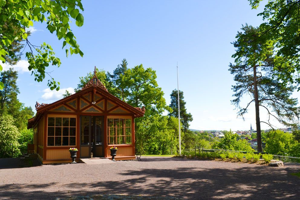 Trepaviljong i en park, omgitt av trær. Solrik dag med utsikt over en by i det fjerne.