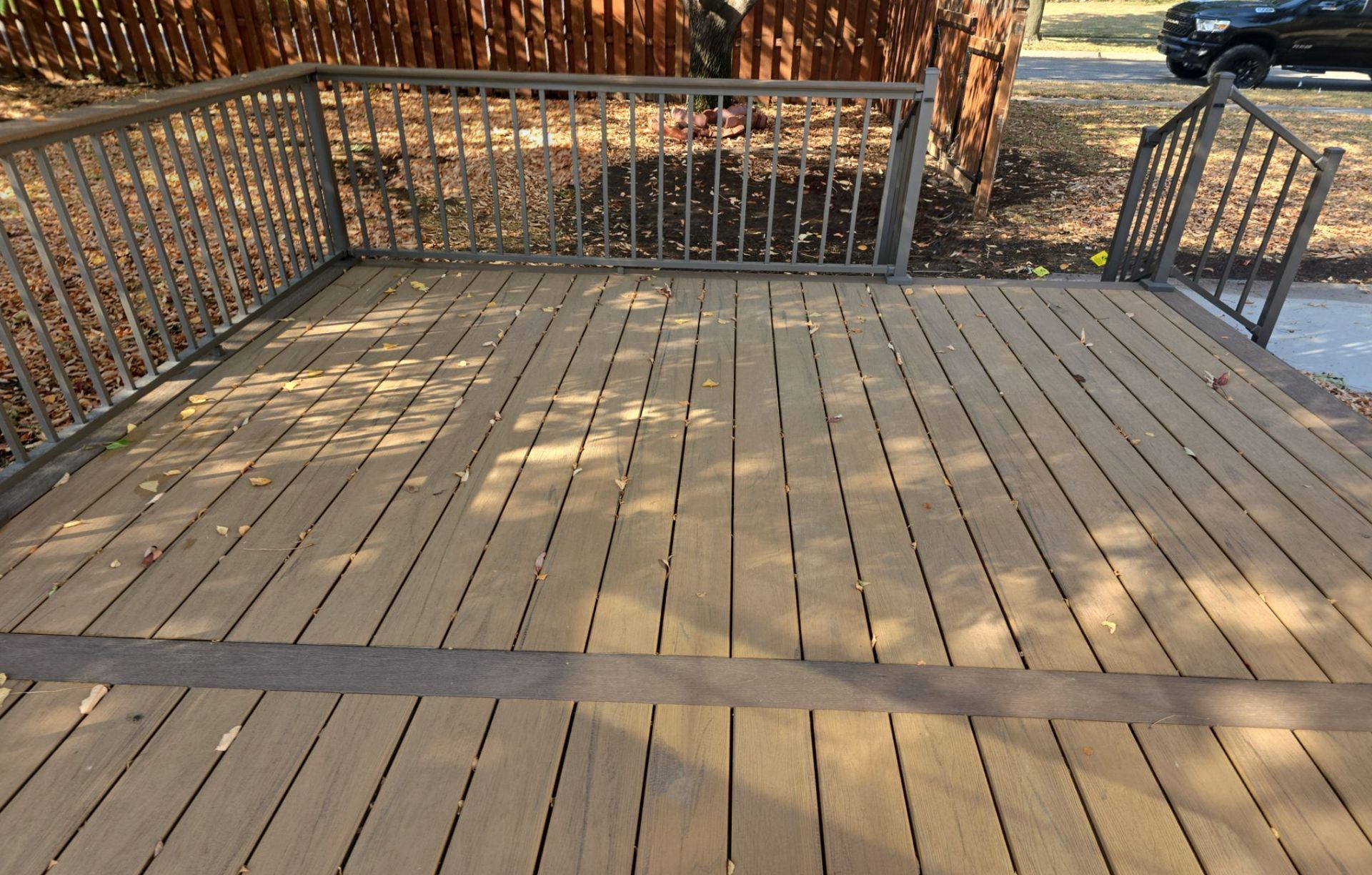 A wooden deck with a metal railing and a car parked in the background.