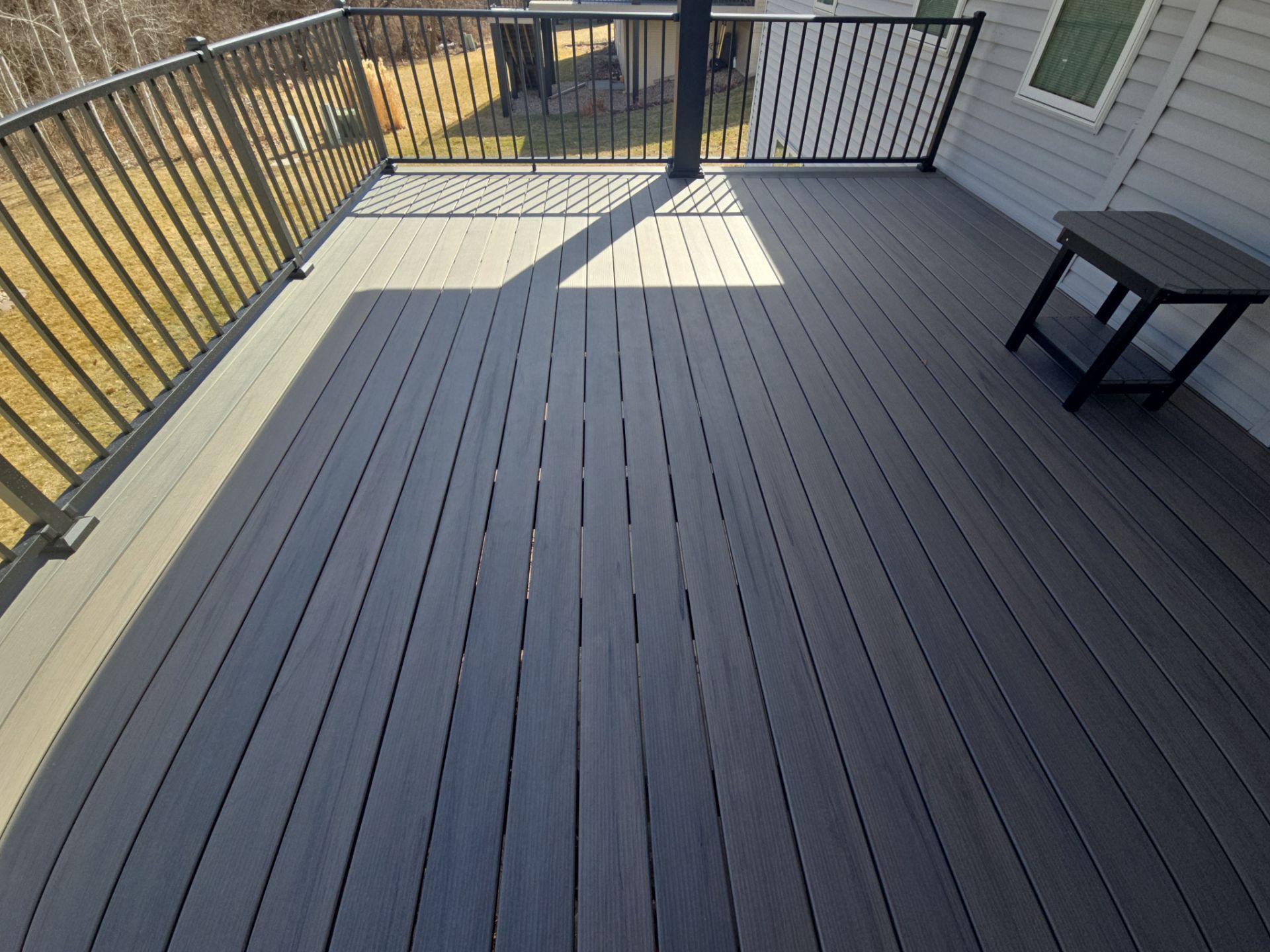 A large composite deck with a metal railing and a table.