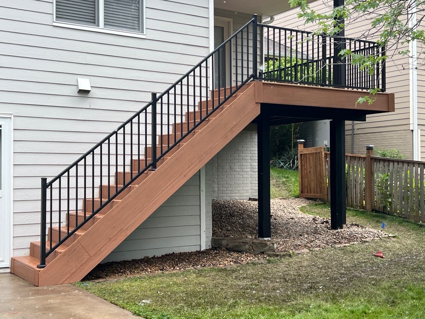 Wooden deck with black railing and stairs leading up from ground level.