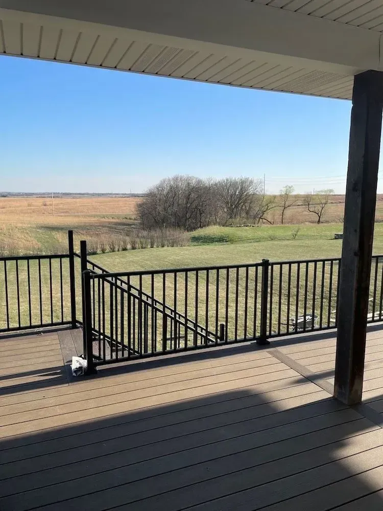 There is a view of a field from the deck of a house.
