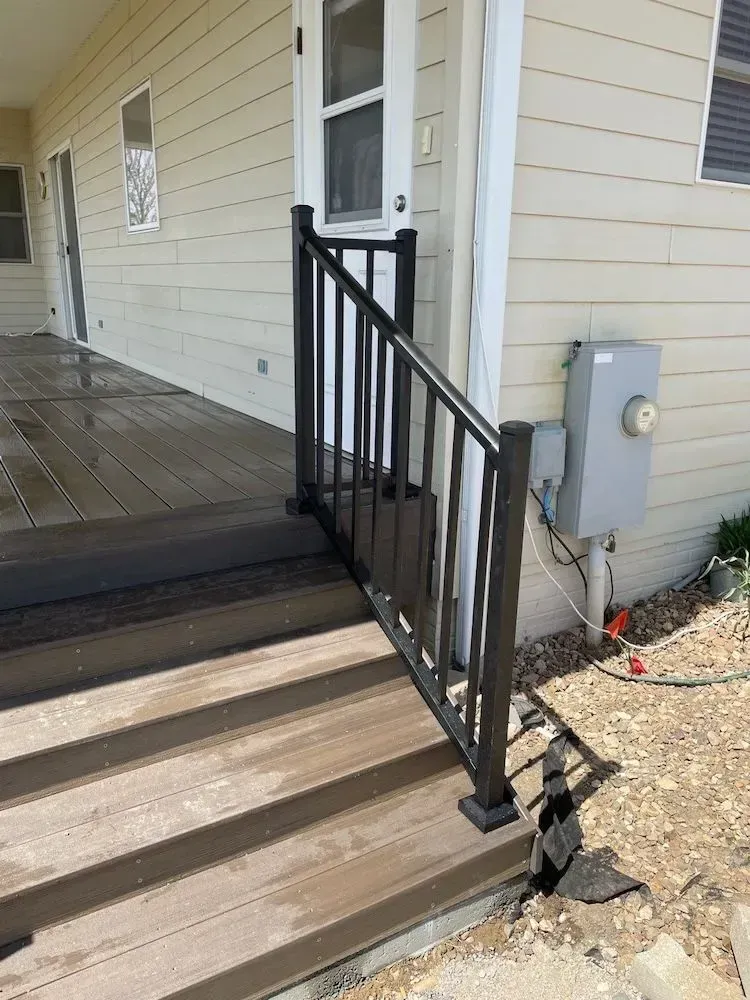 A house with a deck and stairs with a black railing.