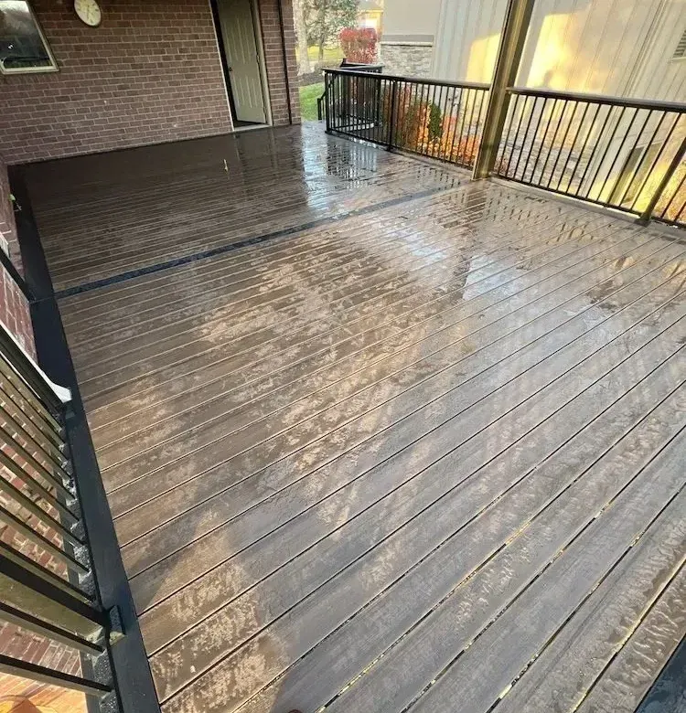 A wooden deck with a railing and a brick building in the background.
