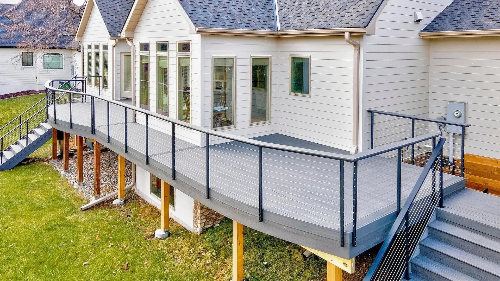 A large deck with stairs leading up to it is in the backyard of a house.