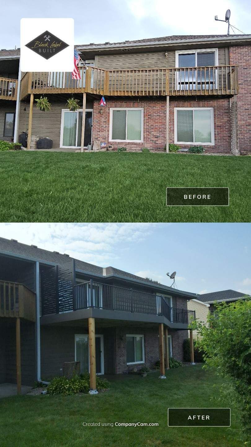 Two-story brick and wood apartment buildings with balconies, a grassy lawn, and a clear sky.