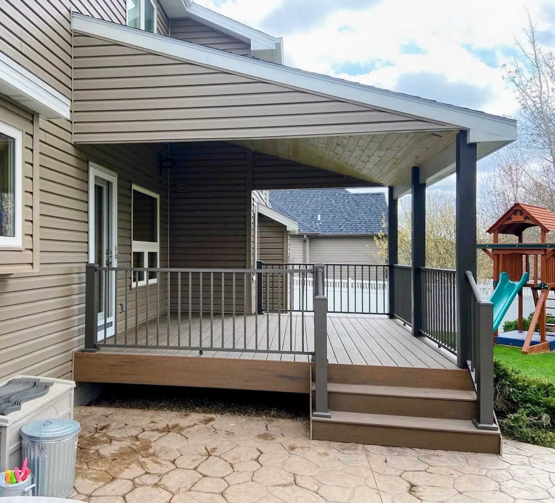 A large deck with stairs and a railing is in the backyard of a house.