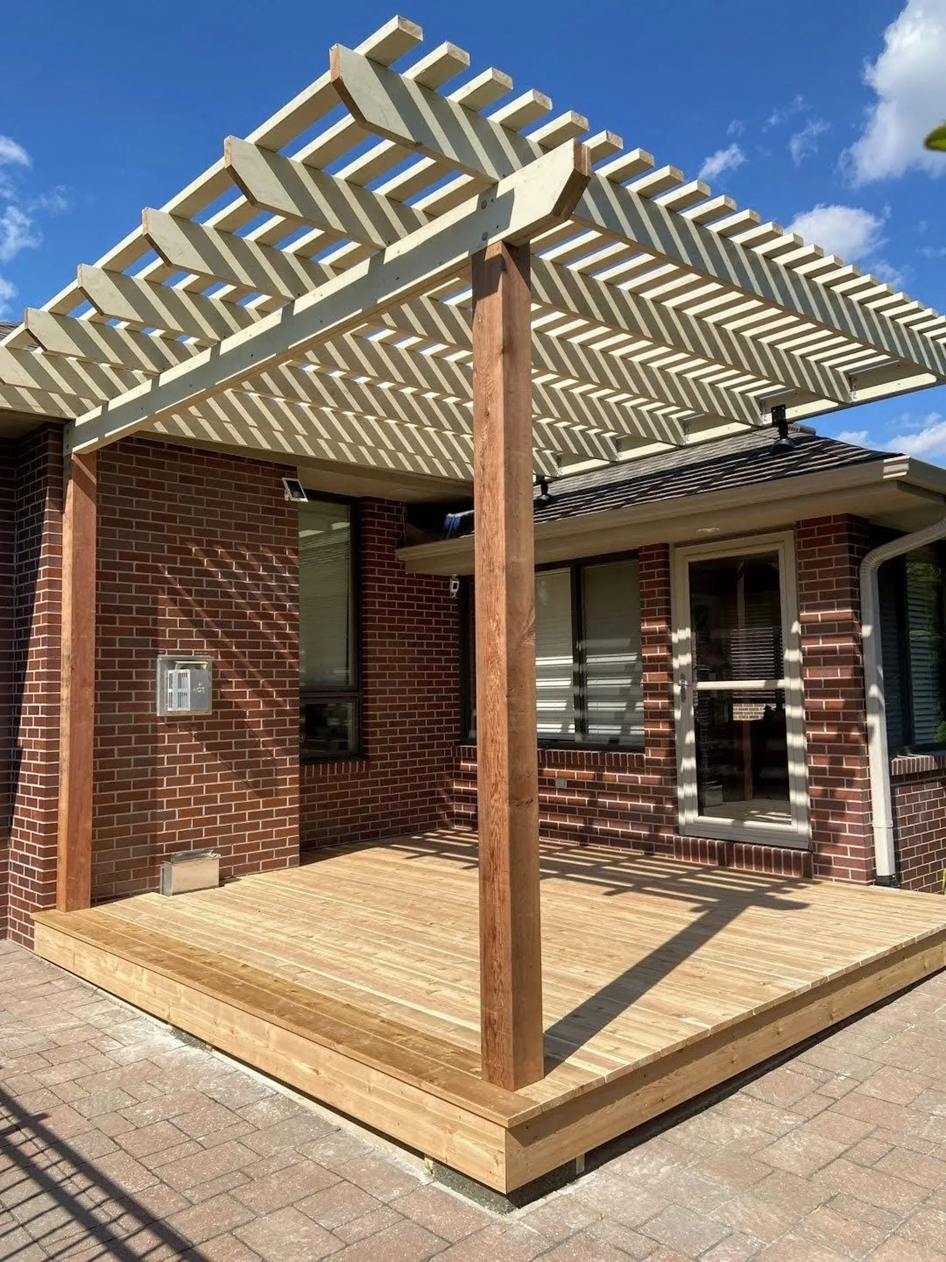 A wooden deck with a pergola over it is in front of a brick house.