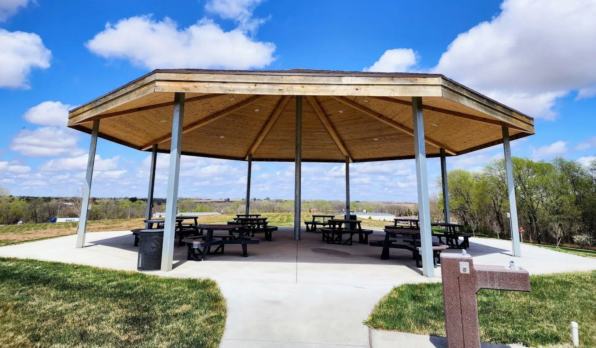 A wooden gazebo with picnic tables underneath it in a park.