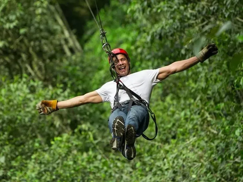 Person ziplining through lush green forest with arms outstretched and a red helmet