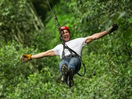 Person ziplining through lush green forest with arms outstretched and a red helmet