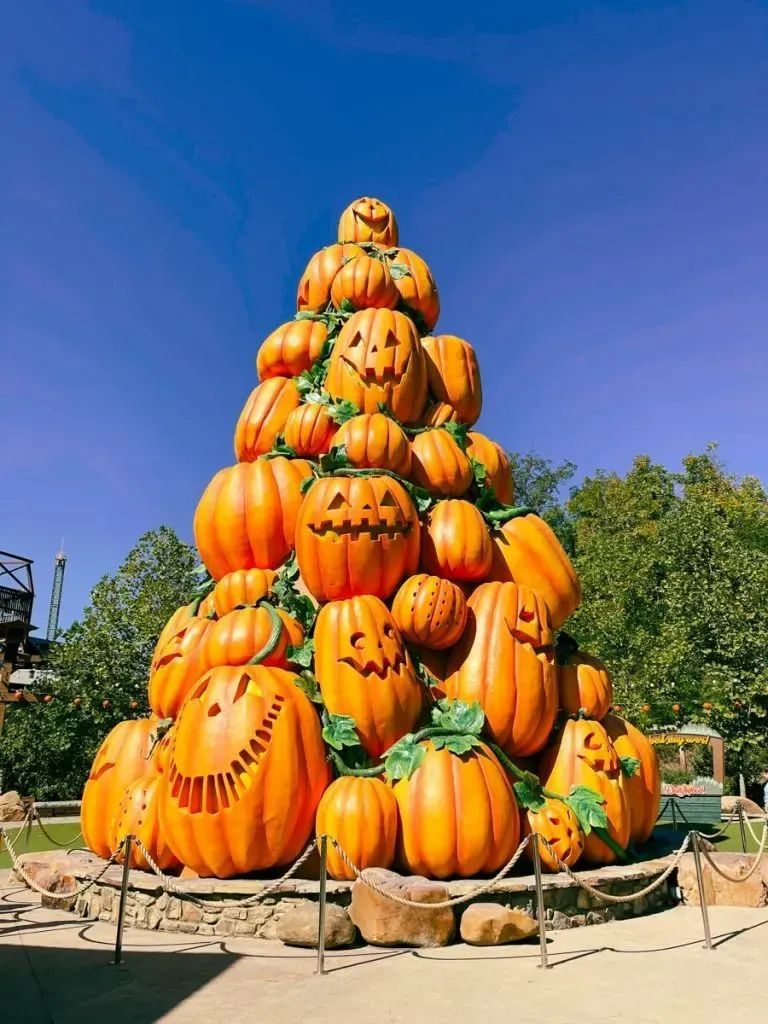 Tall stacked orange pumpkins arranged in a pyramid outdoors against a blue sky
