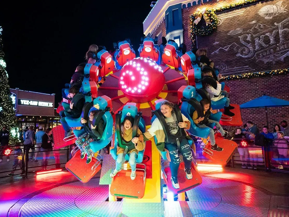 People ride an illuminated, rotating carnival ride at night, with bright red lights and a festive, outdoor setting.