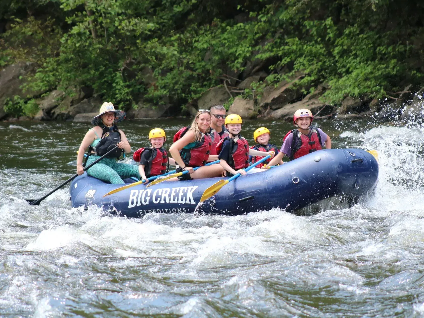 Five people rafting on a whitewater river in a blue inflatable raft