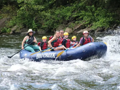 Five people rafting on a whitewater river in a blue inflatable raft