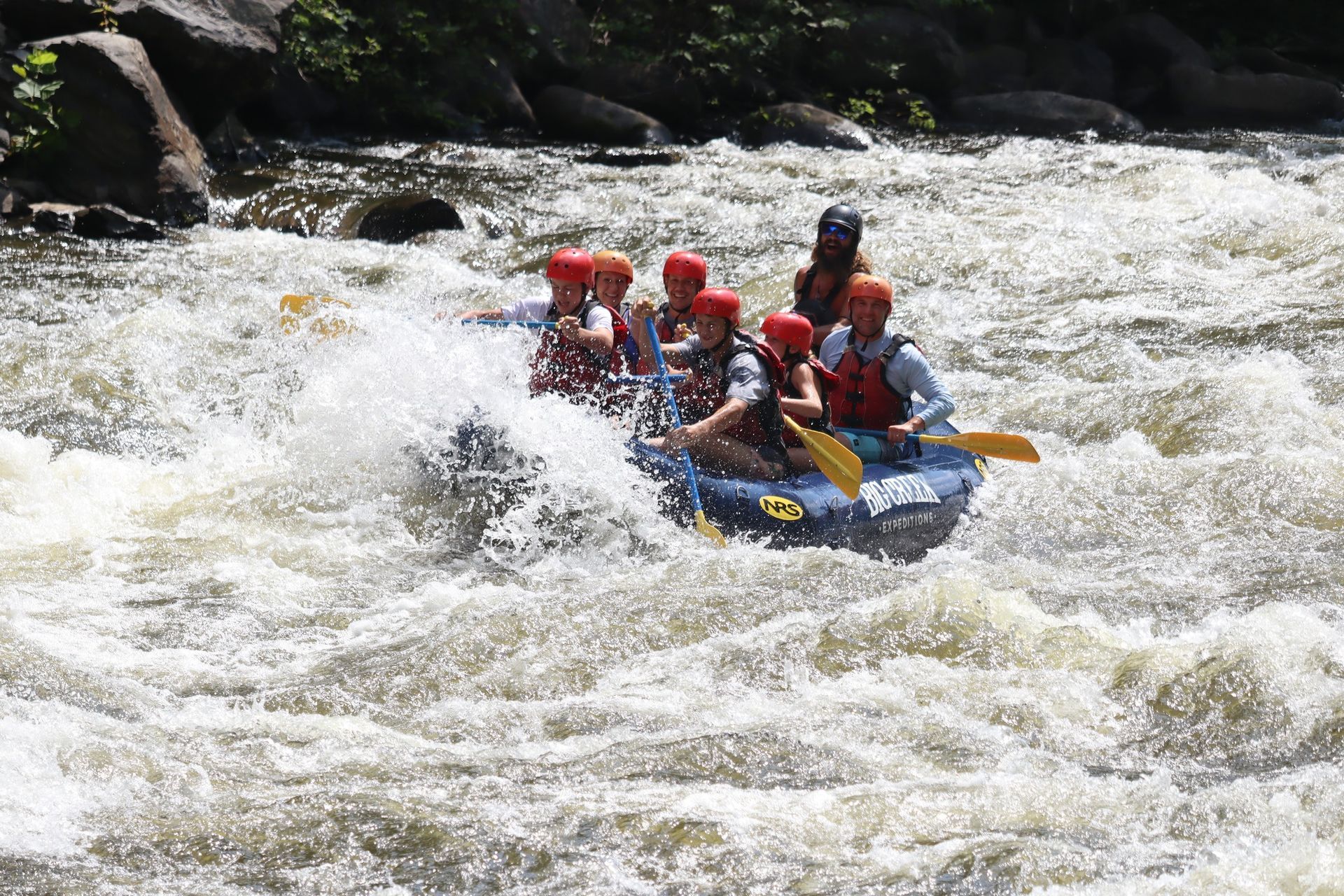 Raft of people in red helmets whitewater rafting through rough rapids