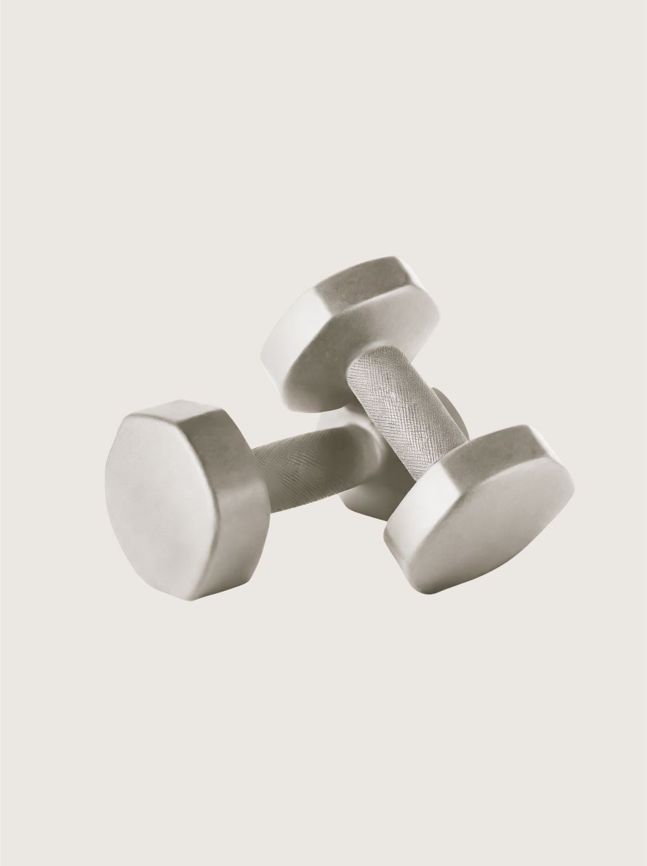 Two gray, hexagonal-shaped metal dumbbells resting crossed on a neutral, off-white background.