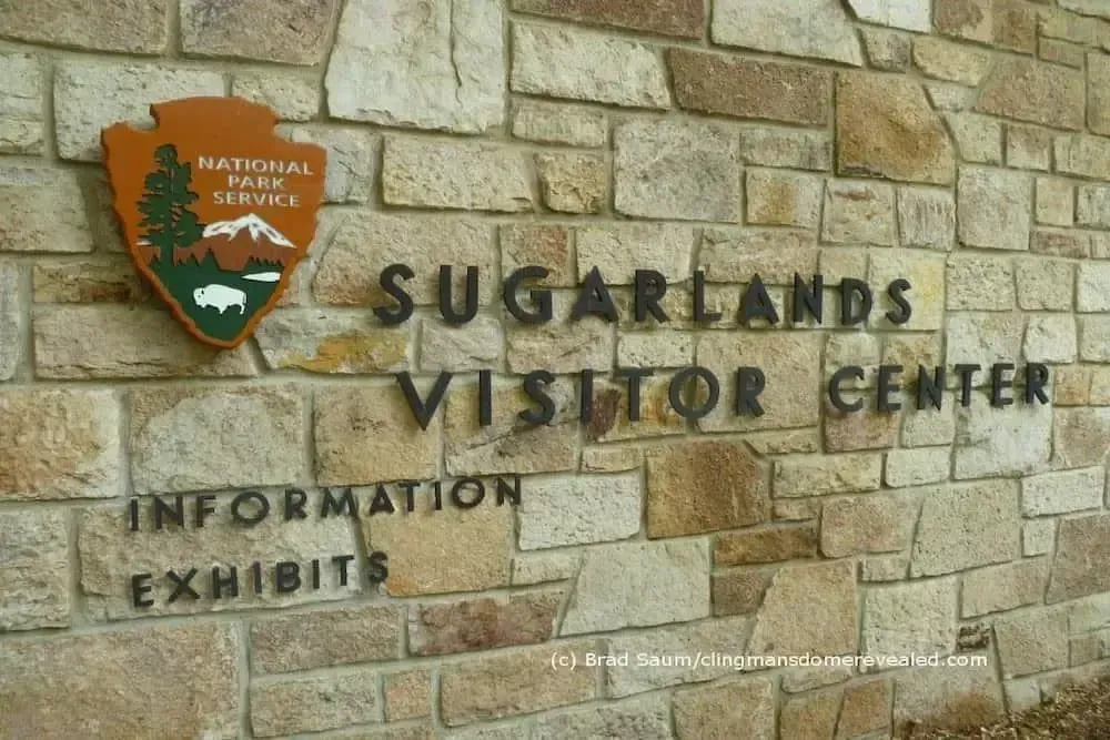 The Sugarlands Visitor Center sign mounted on a rustic stone wall with the National Park Service logo.