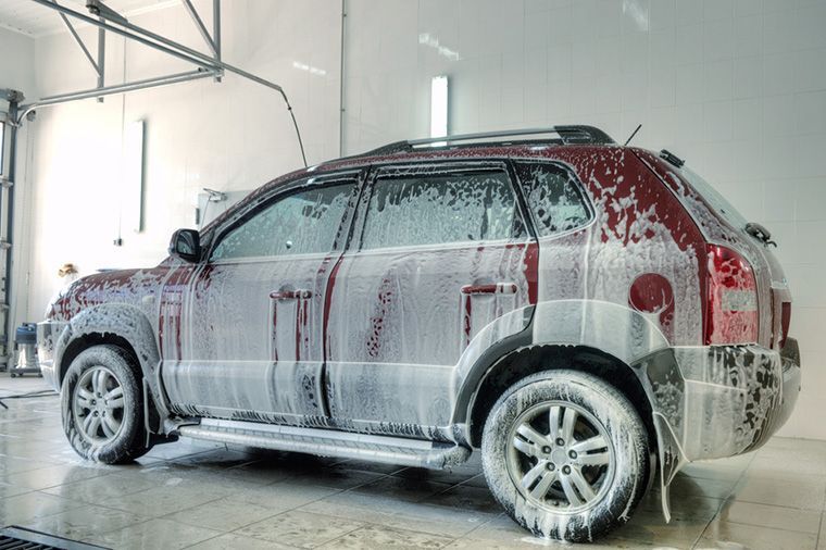 Un suv rouge est recouvert de mousse dans un lave-auto.