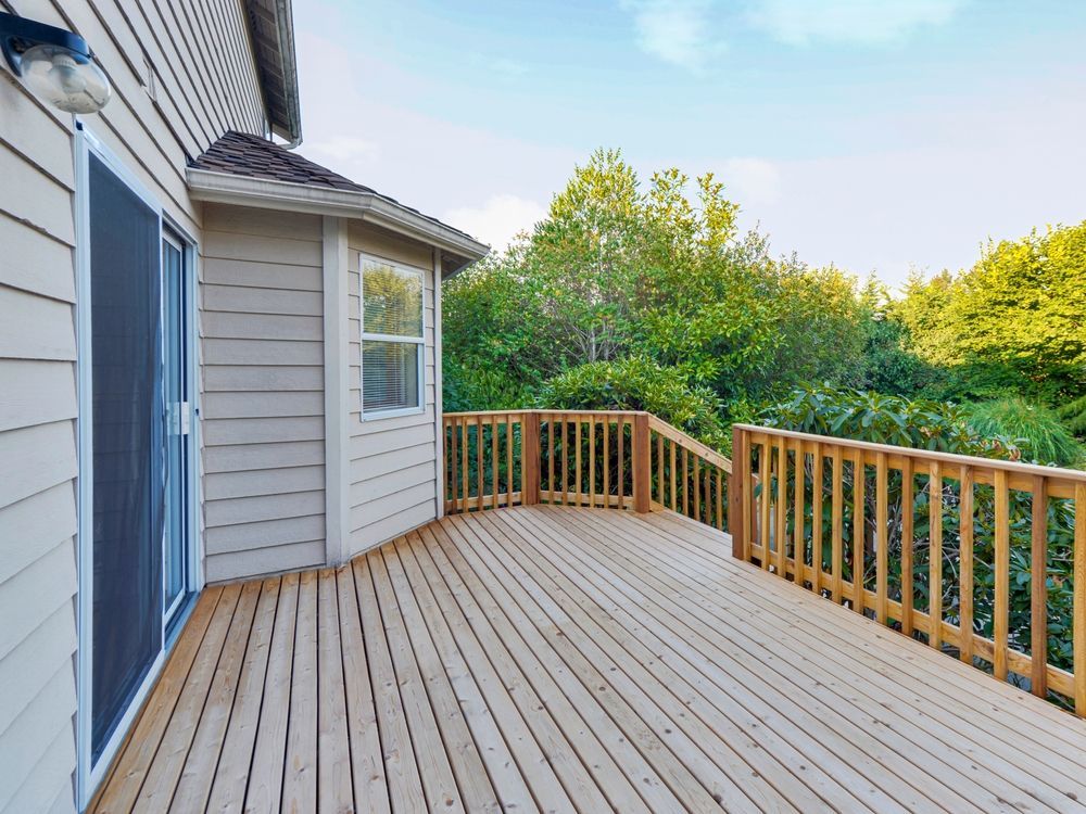 An empty deck with a wooden railing and sliding glass doors on the side of a house.