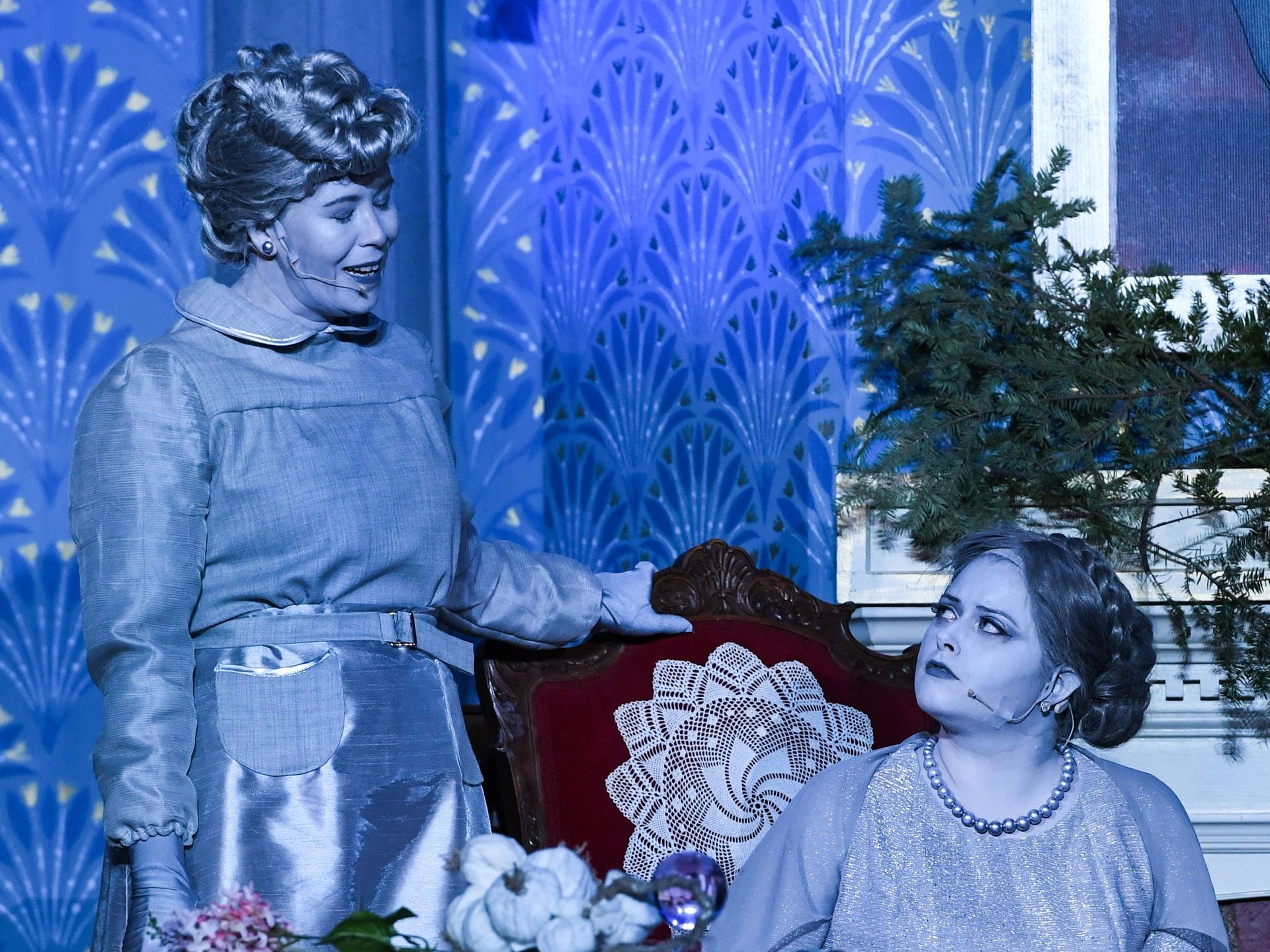 Two women are standing next to each other in front of a blue wall.