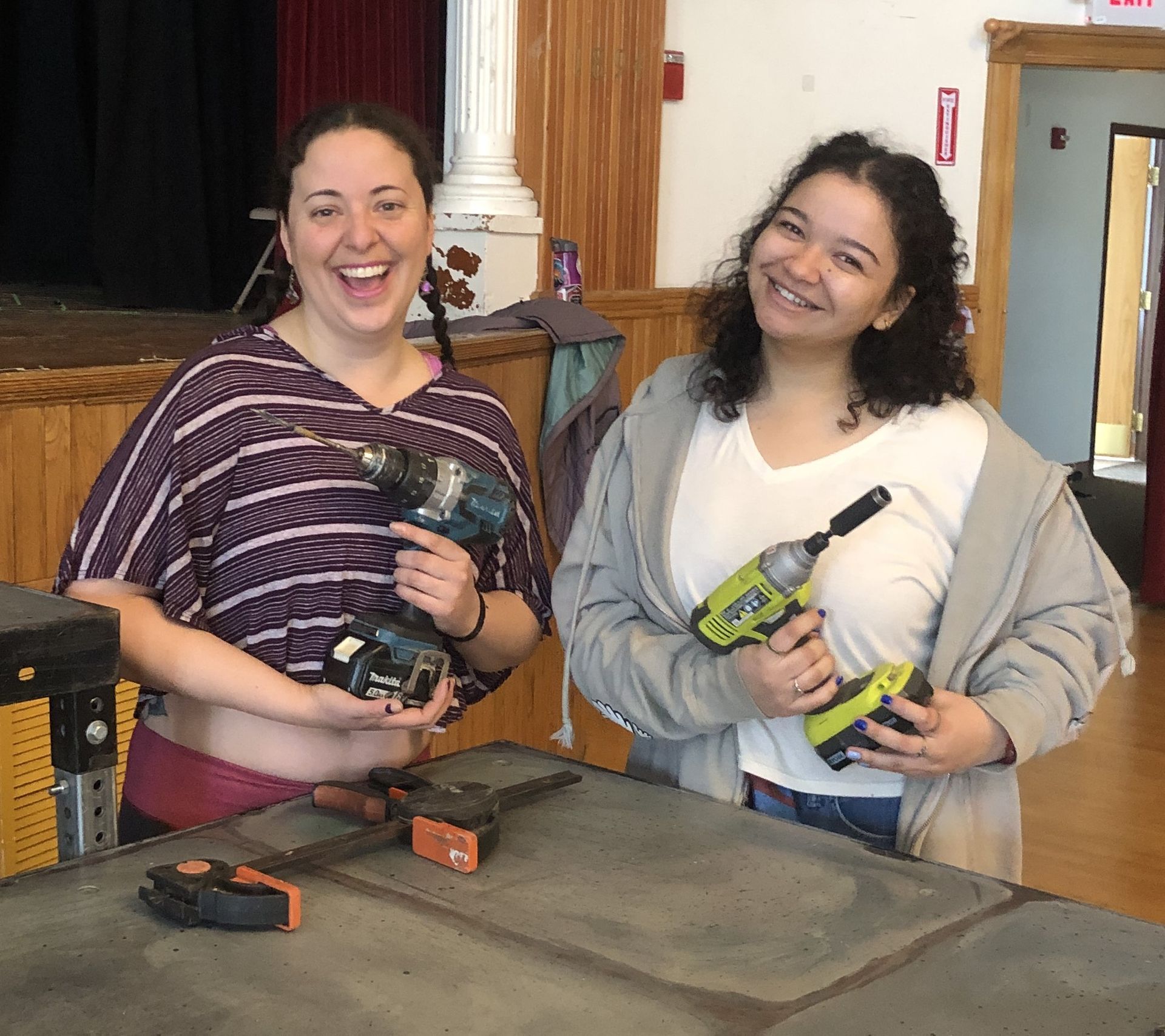 Two women standing next to each other holding tools and smiling