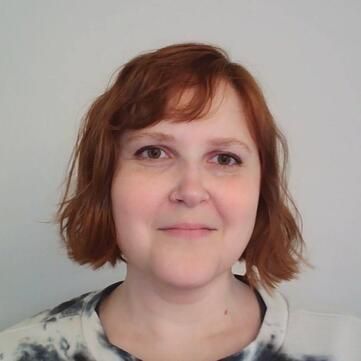 A woman with red hair is smiling and wearing a tie dye shirt.