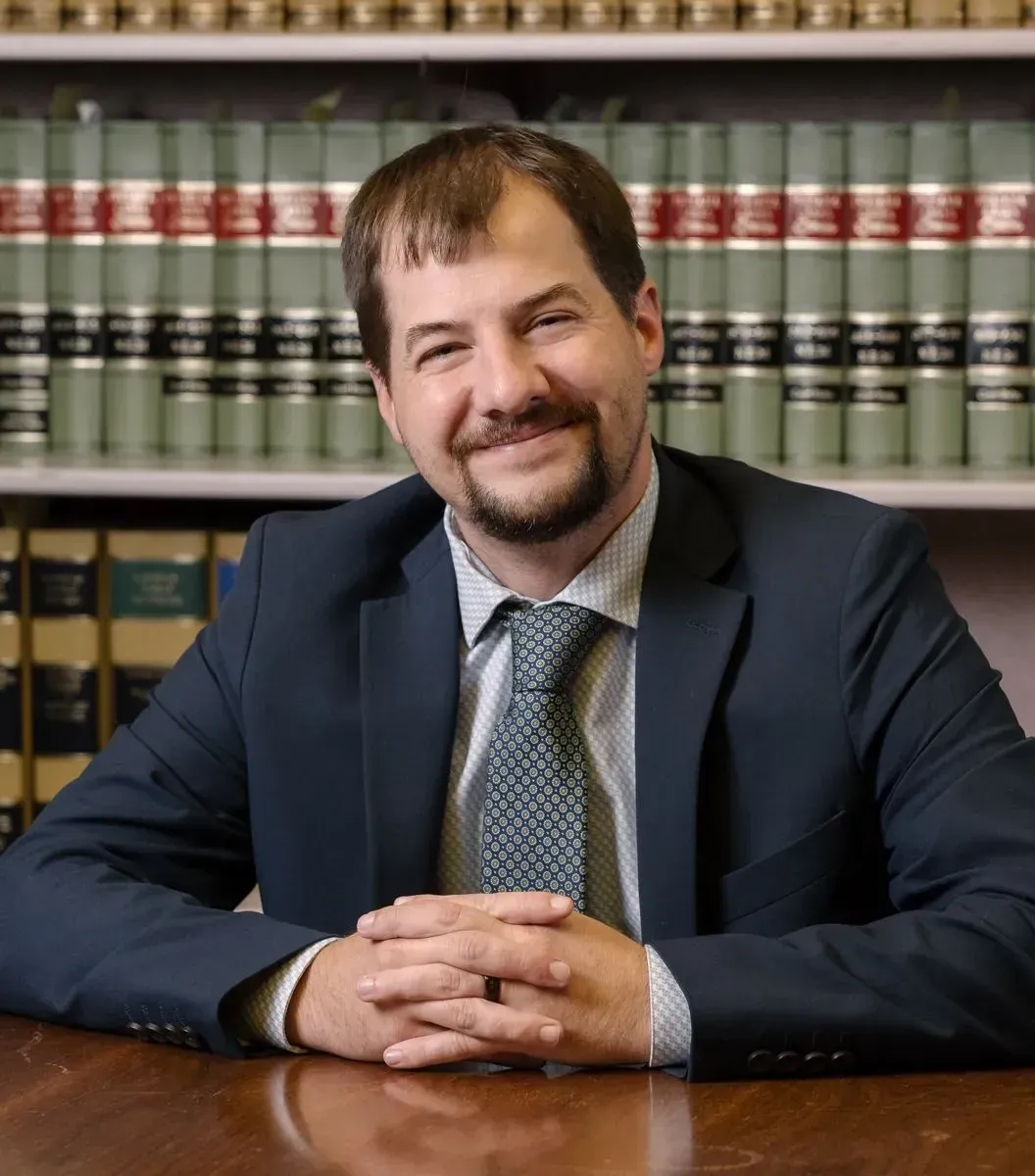 A man in a suit and tie is sitting at a desk with his hands folded