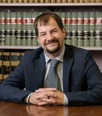 A man in a suit and tie is sitting at a desk with his hands folded