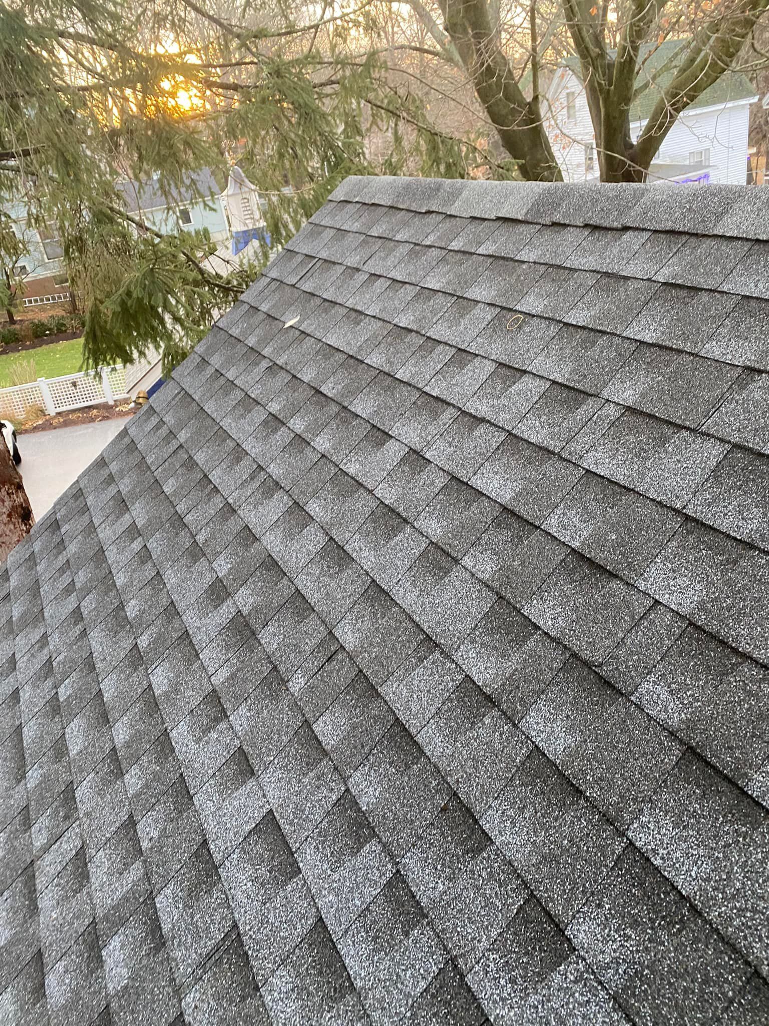 Gray shingle roof of a house with light yellow siding and white trim.