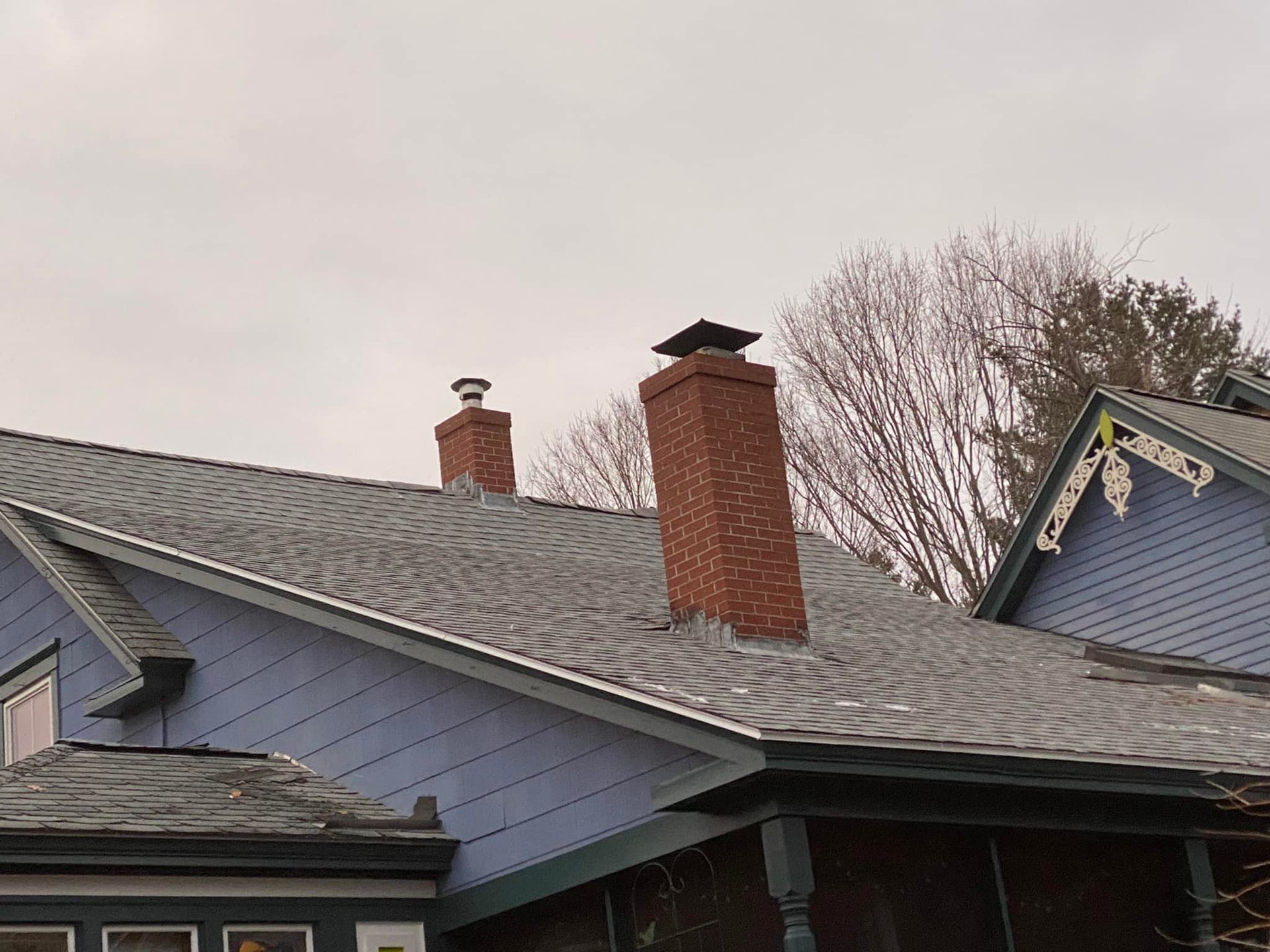 Blue house roof with two brick chimneys under a cloudy sky.