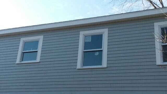 White house with chain-link fence, two windows, and green trash bins.