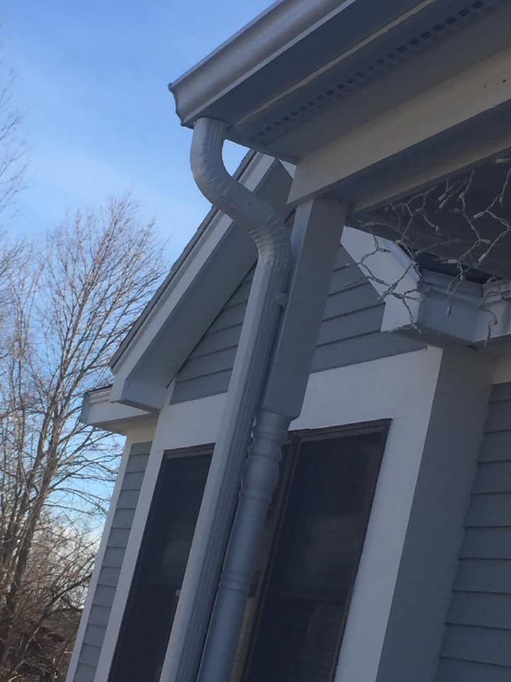 Gutter with mesh screen installed on a roof, next to a gravel surface, with a ladder visible.
