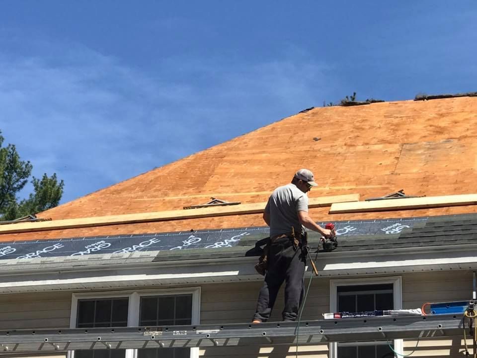 A house roof under construction, with a chimney, dormer, and ladder visible against a cloudy sky.