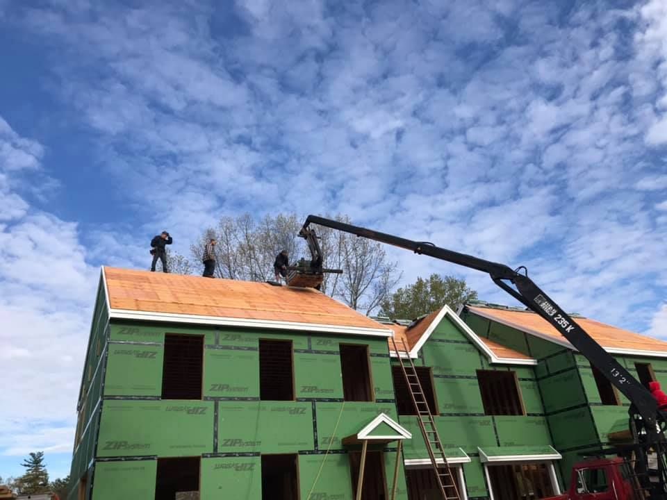 Roofers installing new shingles on a beige house under a clear blue sky.