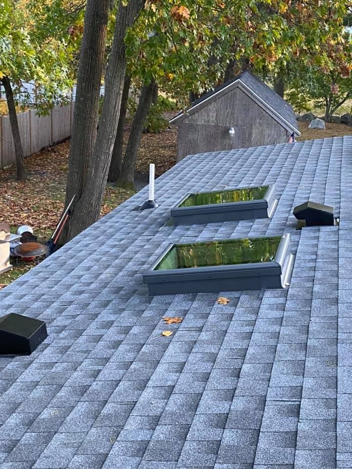 Gray shingled roof with two skylights, a chimney, and a shed in the background.