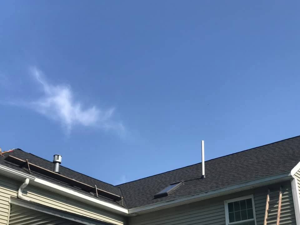 House roof with vent pipe and gutter against a blue sky with some clouds.