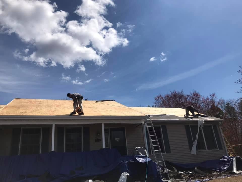 Roofers working on a house roof under a blue sky with clouds.