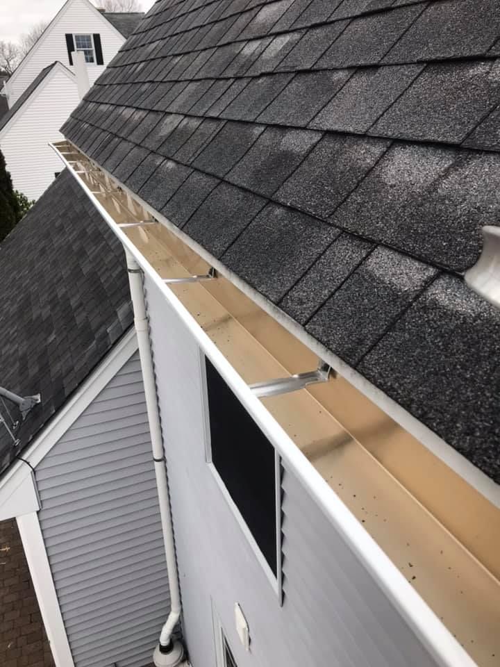Gutter on a roof with gray shingles. Silver supports and tan interior.