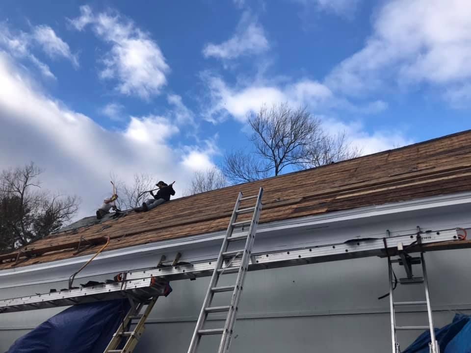 Roofers working on a brown shingle roof under a cloudy blue sky.