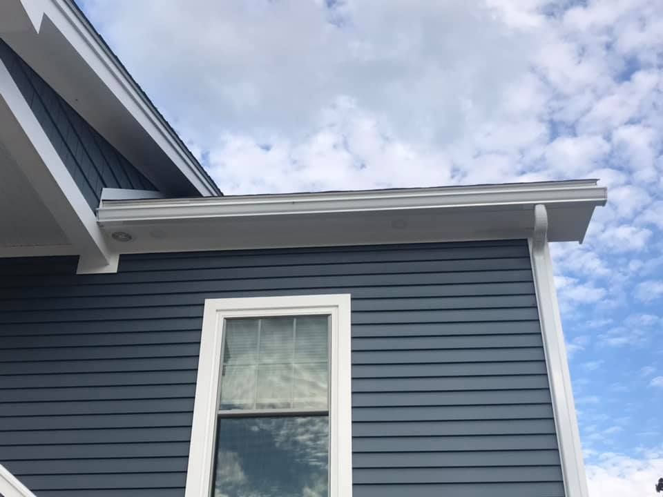 Dark blue house siding with a white-framed window and gutter, against a cloudy sky.