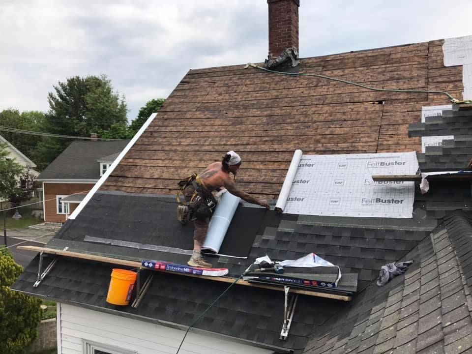 Roofer installing roofing material on a house, working on a sunny day.