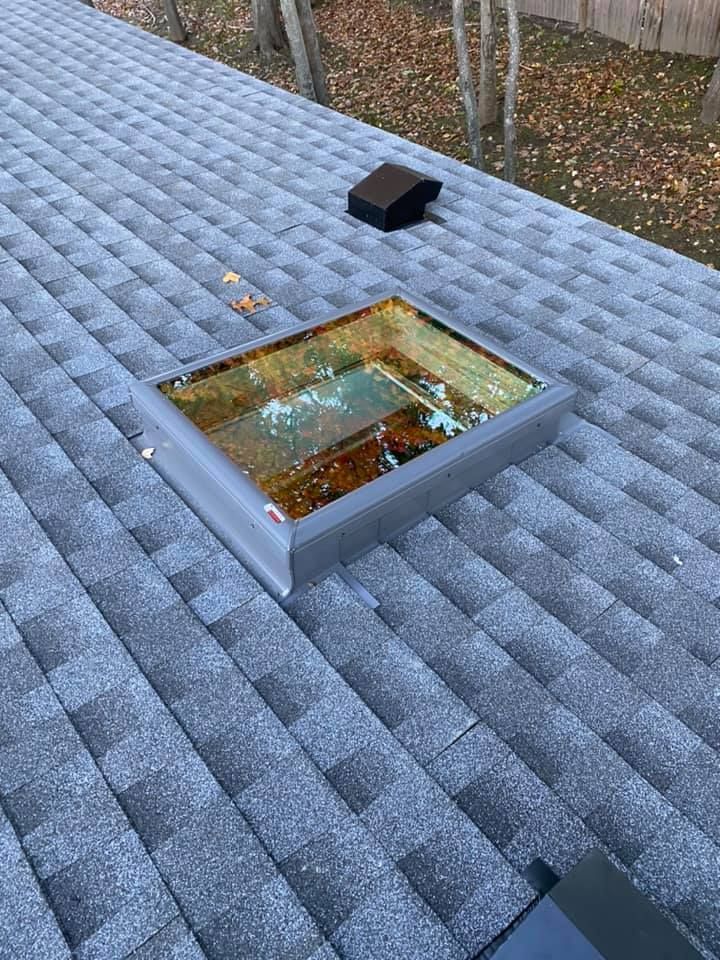 Skylight on a gray shingled roof with a black vent in the background.