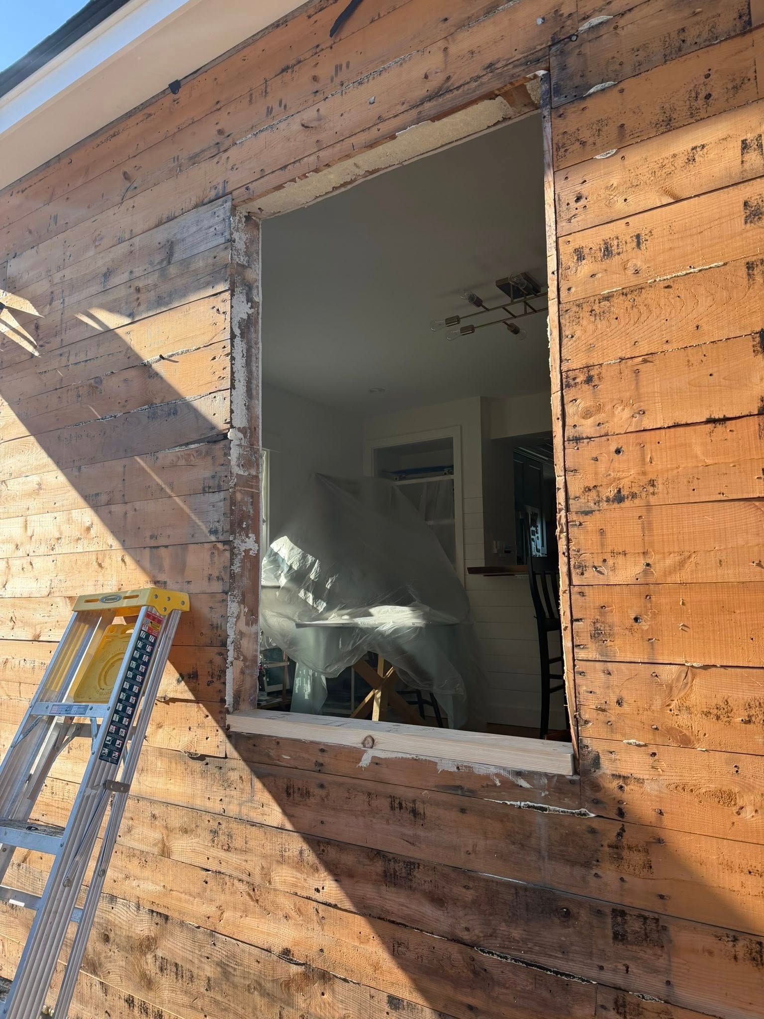 Exterior wall with a large opening, ladder, and a glimpse of an interior room.