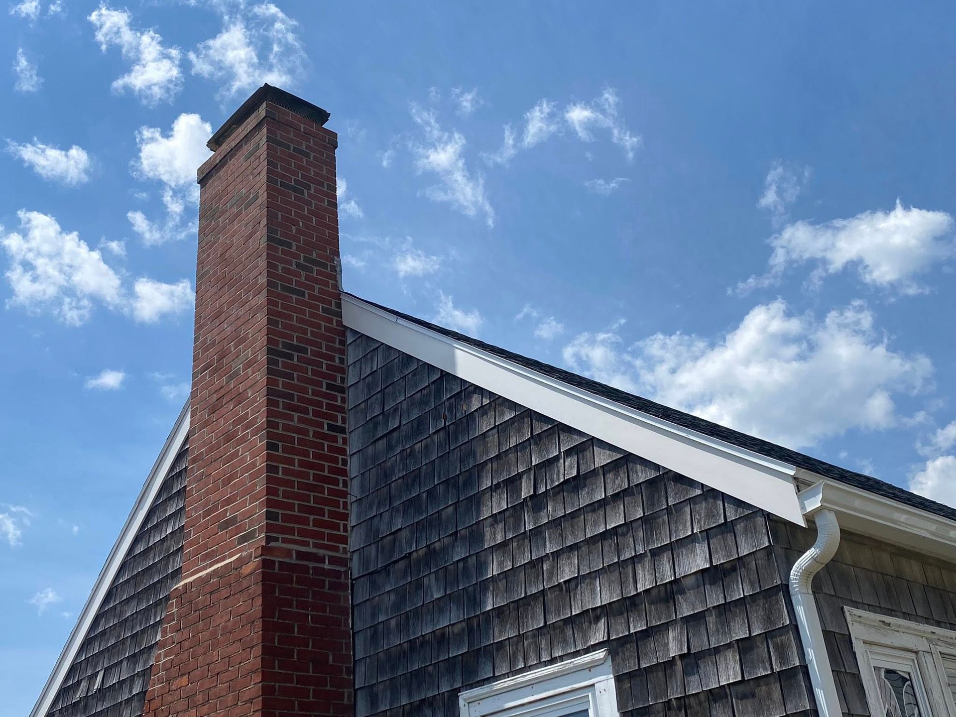 Brick chimney against a blue sky, beside a wood-shingled roof.