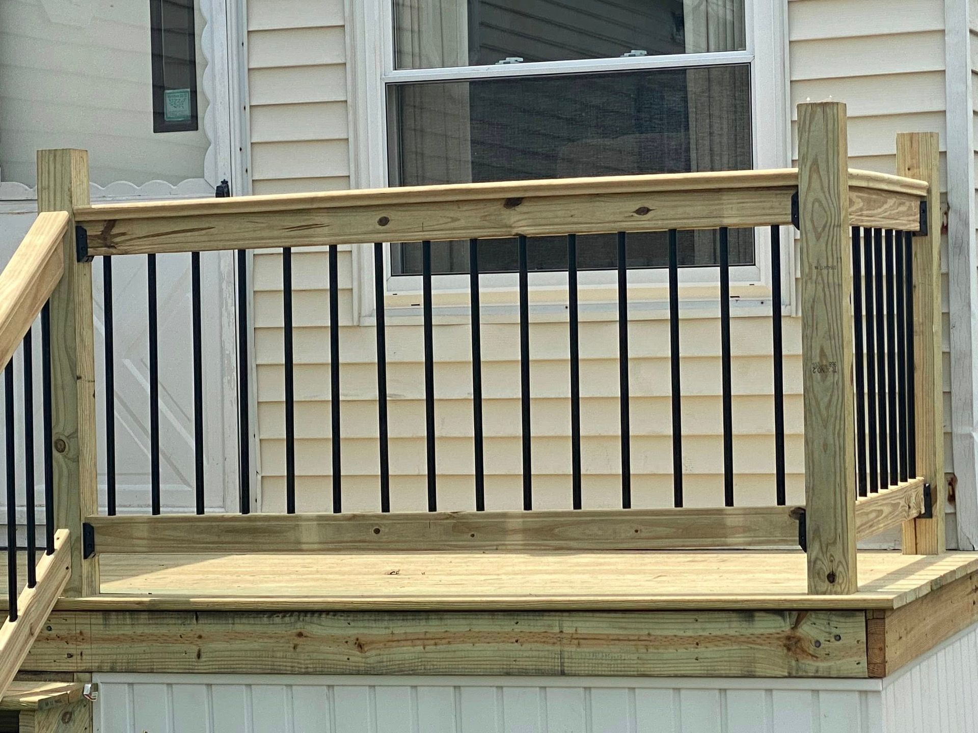 Wooden deck with black metal railing in front of a window.