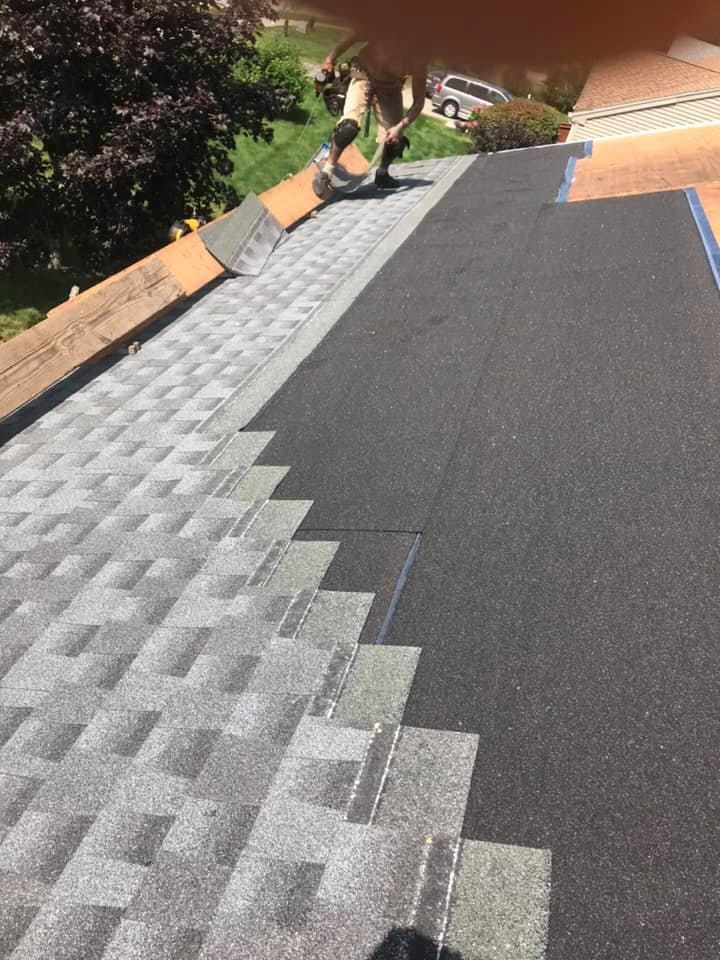 Roof shingles being installed, partially complete, with worker visible. 