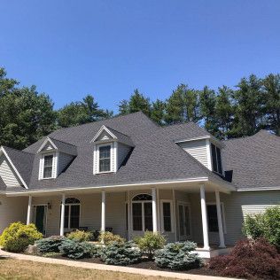 Beige house with gray roof, white trim, and dormers under a clear, blue sky.
