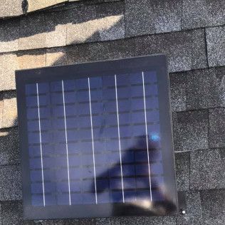 Small solar panel mounted on a dark shingle roof, with a reflection on its surface.