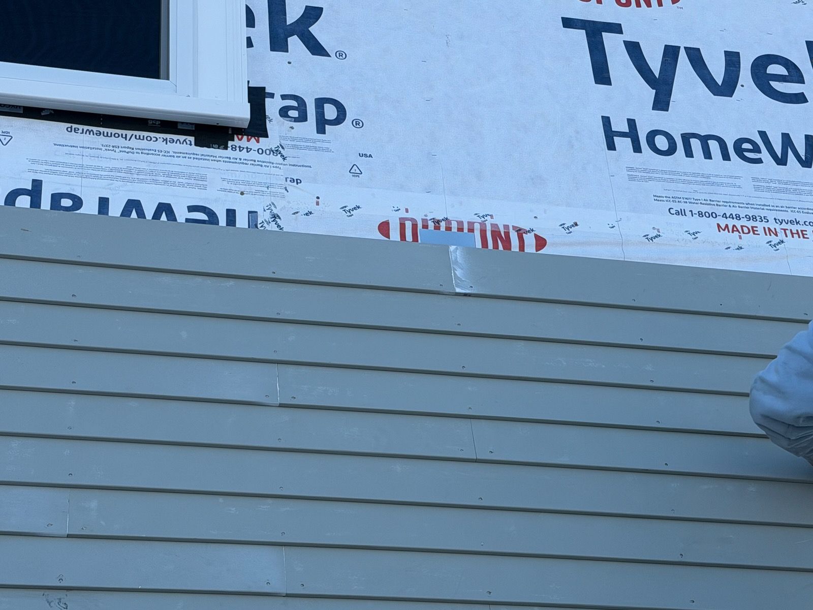 Beige house exterior with white trim and windows against a blue sky.